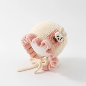 Detailed close-up of knitted baby bonnet with pink ruffle trim and rabbit patch