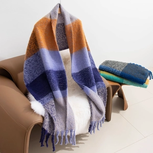 Detail of soft mohair plaid scarf with fringes draped on a brown leather chair