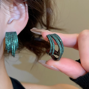Close-up of elegant emerald green cubic zirconia multi-row hoop earrings on model.