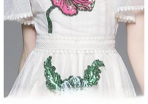 Détail d'une robe en tulle blanc avec broderies florales à paillettes colorées et taille ajustée