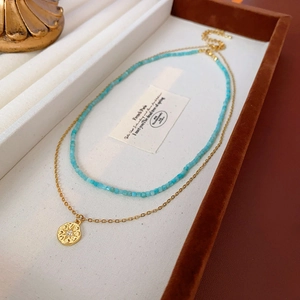 Détail du collier doré avec pendentif ajouré et perles bleues dans un écrin à bijoux