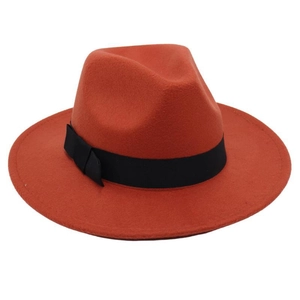 Detail of rust red wool fedora hat featuring a black ribbon band and bow decoration