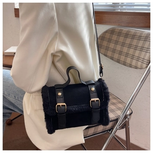 Close-up of black suede cylinder bag with plush trim and golden buckles in a cafe