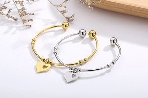Detail of gold and silver heart pendant bangles with sliding beads on white background