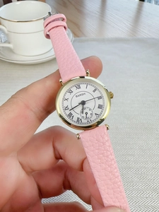 Detail of pink leather strap and gold watch case with Roman numeral dial held by hand