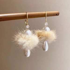Macro shot of elegant earrings with beige pom poms and teardrop pearl drops on wood