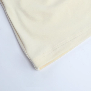Détail du tissu tricoté blanc crème montrant l'ourlet à double couture et la texture