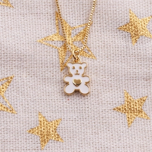 Macro d'un pendentif ours en émail blanc avec cœur doré sur une chaîne maille