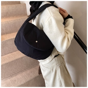 Detail of a black quilted puffer shoulder bag with a silver magnetic button on the flap