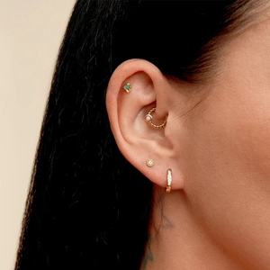 Detail of ear piercings with gold studs and hoops featuring green and pink gemstones