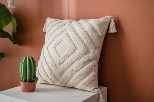 Close-up of tufted geometric diamond pattern and corner tassels on cream boho pillow