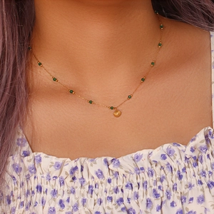 Detail of golden shell pendant necklace with green beads worn on model's neck