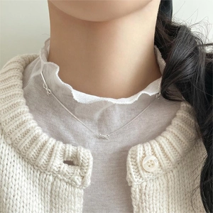 Detail of silver bow pendant necklace worn by a model with a knit sweater background