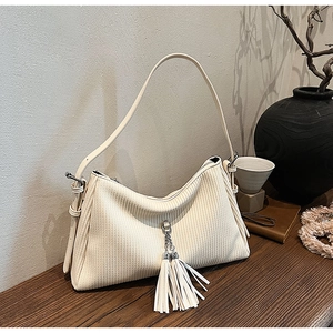 Detail of cream corduroy shoulder bag featuring decorative long metal tassel chains