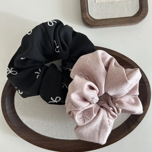 Pink and black fabric bow scrunchies with elegant floral embroidery on a wooden tray
