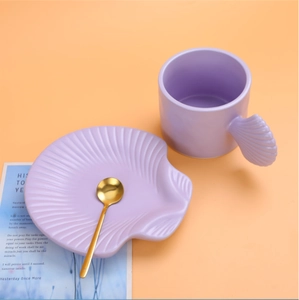 Detailed view of a purple ceramic mug with a shell handle on a matching saucer with a gold spoon