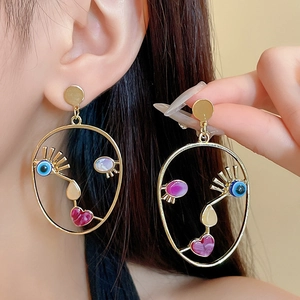 Artistic golden face outline earrings with colorful resin details worn by a model