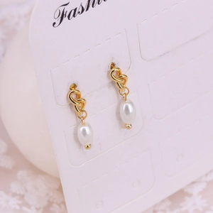Macro view of elegant gold knot and oval pearl drop earrings on a fashion display card