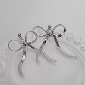 Detailed view of silver bow tassel earrings crafted with snake chain on glass plate