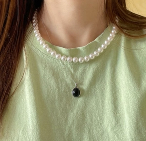 Detail of layered jewelry set with white pearl choker and black oval pendant necklace