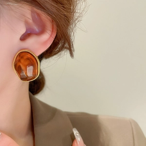Close-up of geometric amber resin earrings with a twisted gold metal border on a model