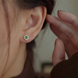Close-up of petal-shaped earrings with a green center gemstone and pavé diamonds