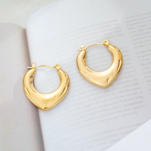 Detailed close-up of 18K gold plated heart earrings with hammered texture on magazine
