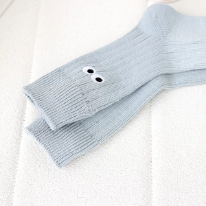 Close-up of light blue knitted socks featuring cute cartoon eye embroidery on the cuff