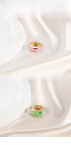 Detail view of adjustable gold rings with pink enamel and green natural stone inlay
