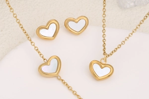 Macro shot of gold heart jewelry set with white mother of pearl inlay on white base