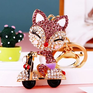 Detail of fox on scooter keychain featuring pink rhinestones and enamel on gold metal