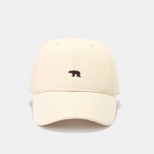 Detail of minimalist cream cotton baseball cap featuring a small brown bear embroidery