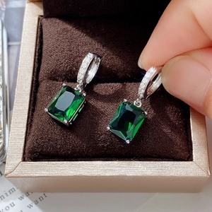 Macro view of green rectangular zircon earrings with silver diamond-set hooks in a jewelry box