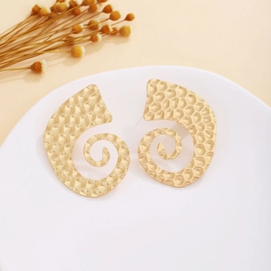 Detail of matte gold spiral earrings with hammered texture on a white ceramic tray