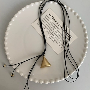 Detail view of a gold geometric triangle pendant with black long adjustable cord on a tray