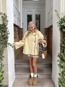Detail of cream cape jacket featuring black contrast stitching and button closure