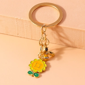 Close-up of golden bee keychain with sunflowers and crystals on a textured beige block
