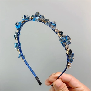 Dettaglio di cristalli blu reale su cerchietto in tessuto con griffe in metallo oro