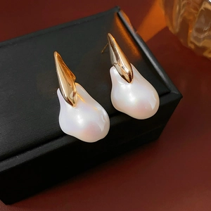 Detail of gold-plated earrings with large irregular white baroque pearls on black display