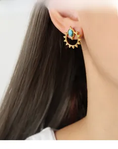 Close-up of bohemian gold earrings with turquoise stone worn by a model