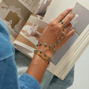 Detailed view of boho turquoise slave bracelet and gold hammered cuff on model holding a book