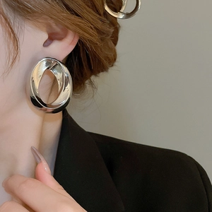Close-up of a model wearing large silver geometric twisted earrings with a polished finish
