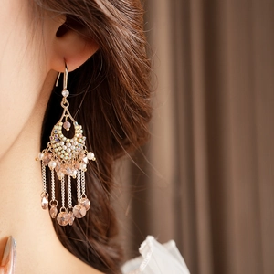 Close-up of golden crescent earrings with colorful gems, pearls and crystal tassels
