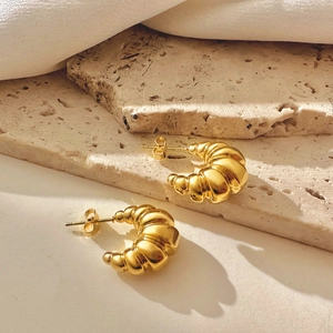 Macro view of 18k gold croissant earrings with ribbed texture on travertine stone