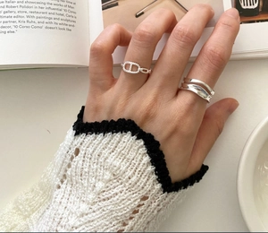 Close-up of silver wavy curved ring and anchor chain band worn on hand with art book