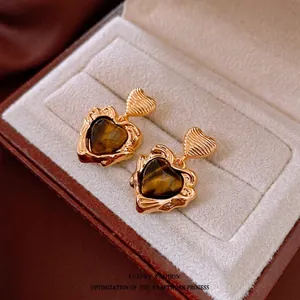 Boucles d'oreilles cœur dorées avec œil de tigre dans un coffret à bijoux rouge