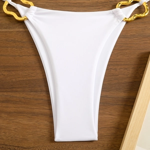 Detail of white bikini bottoms featuring wavy gold metal hardware on wood background