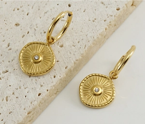 Macro detail of gold hoop earrings with sunburst compass pendant and sparkling crystal