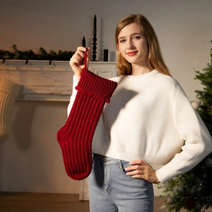 Knitted red Christmas stocking with tassel hanging on a decorated fireplace mantel