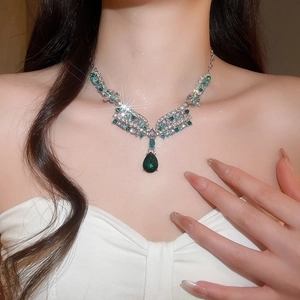 Close-up of a luxurious silver necklace with blue and pear-shaped green gemstones on model